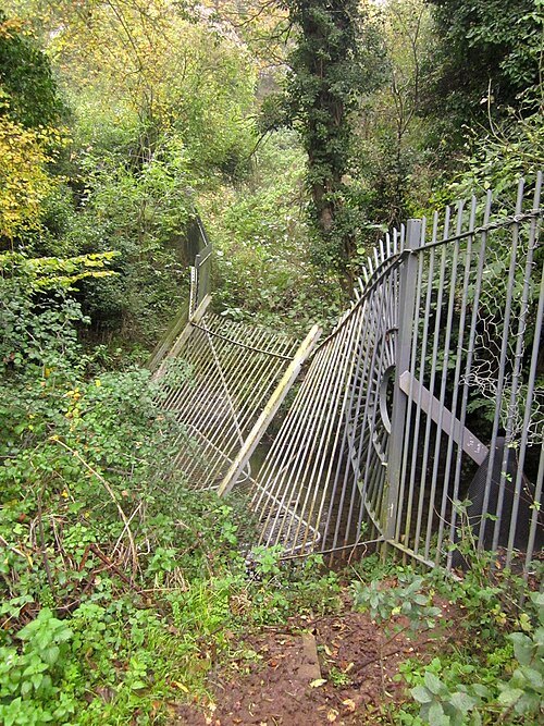 A damaged metal fence leaning into vegetation