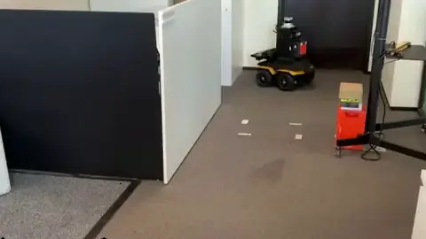 A Clearpath Jackal drives between office desks and through a narrow passage