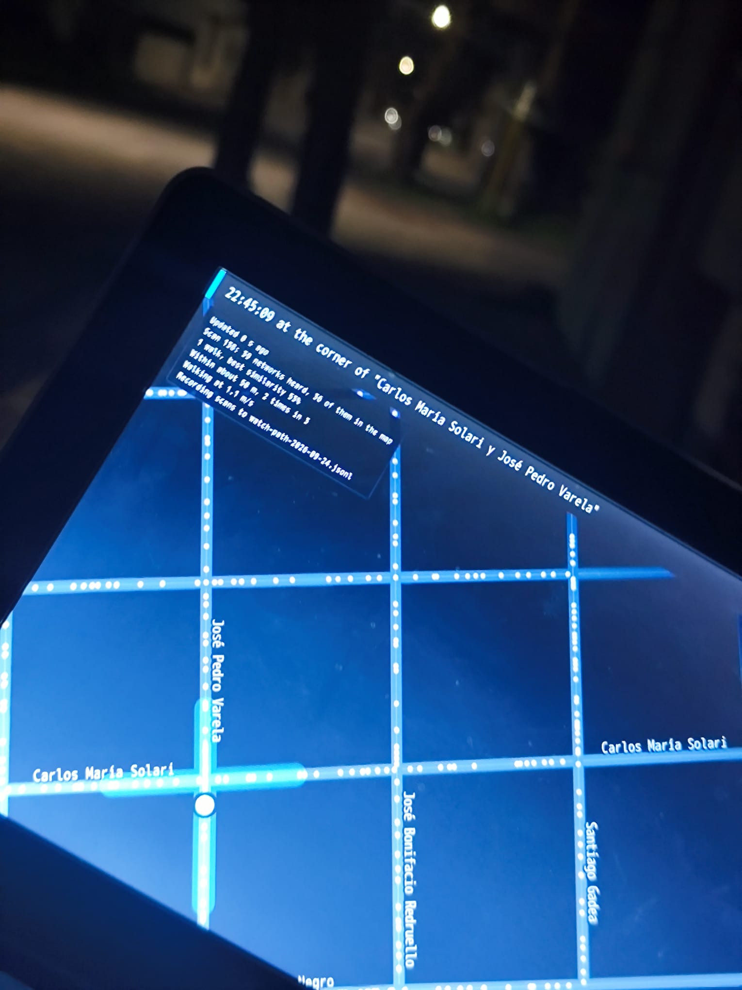 The live map on a laptop at the same corner, at night: the dot on the crossing of José Pedro Varela and Carlos María Solari, the streets around it named, and at the top, 22:45:09 at the corner of Carlos María Solari y José Pedro Varela.